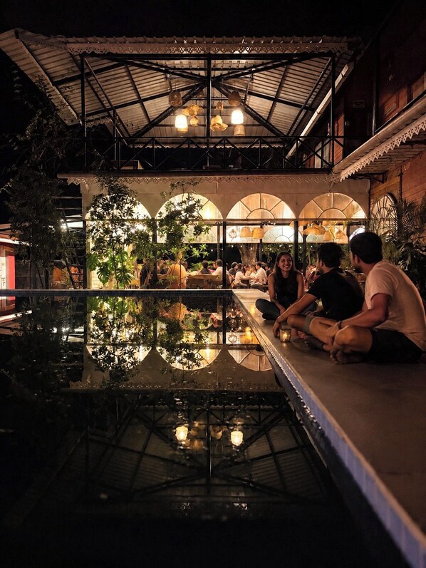 An indoor dining area with a reflective pool, seating arrangements, and a covered roof structure.