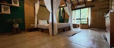 A room with a four-poster bed, wooden flooring, a green accent wall, and a window with a view of trees.