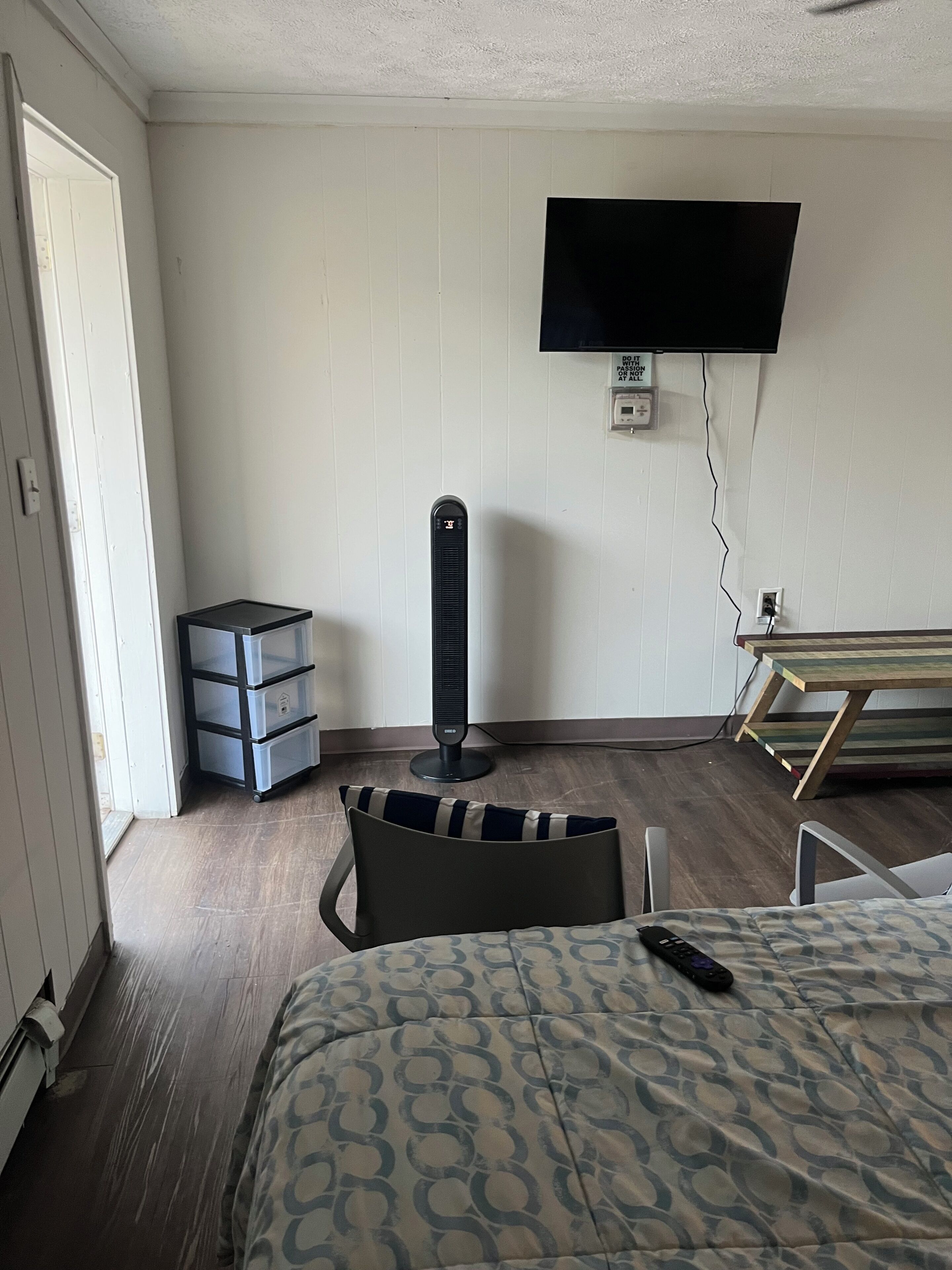 Ett hotellrum med en säng, en tv som är monterad på väggen, ett skrivbord och en stol.