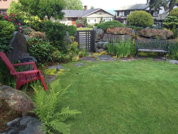 Un jardin bien entretenu, avec une pelouse, une chaise rouge et un mur de pierres.