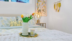 Une chambre à coucher avec un lit, un vase de fleurs, une table de chevet avec une lampe et une œuvre d’art murale.
