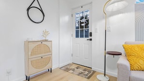 Une pièce avec un meuble en bois, une porte blanche, un lampadaire et un canapé agrémenté d’un coussin jaune.