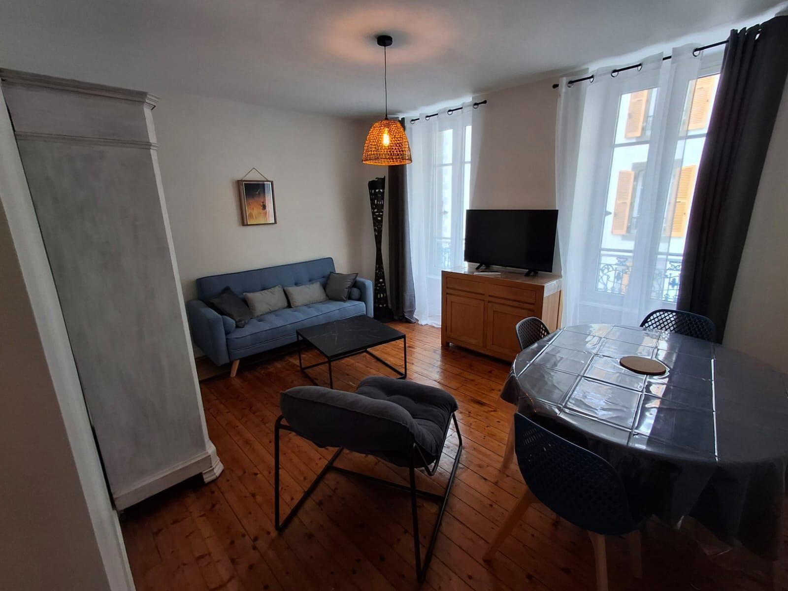 Un salon comprenant un canapé, une table basse, une table à manger avec des chaises, un téléviseur et une fenêtre avec des rideaux.