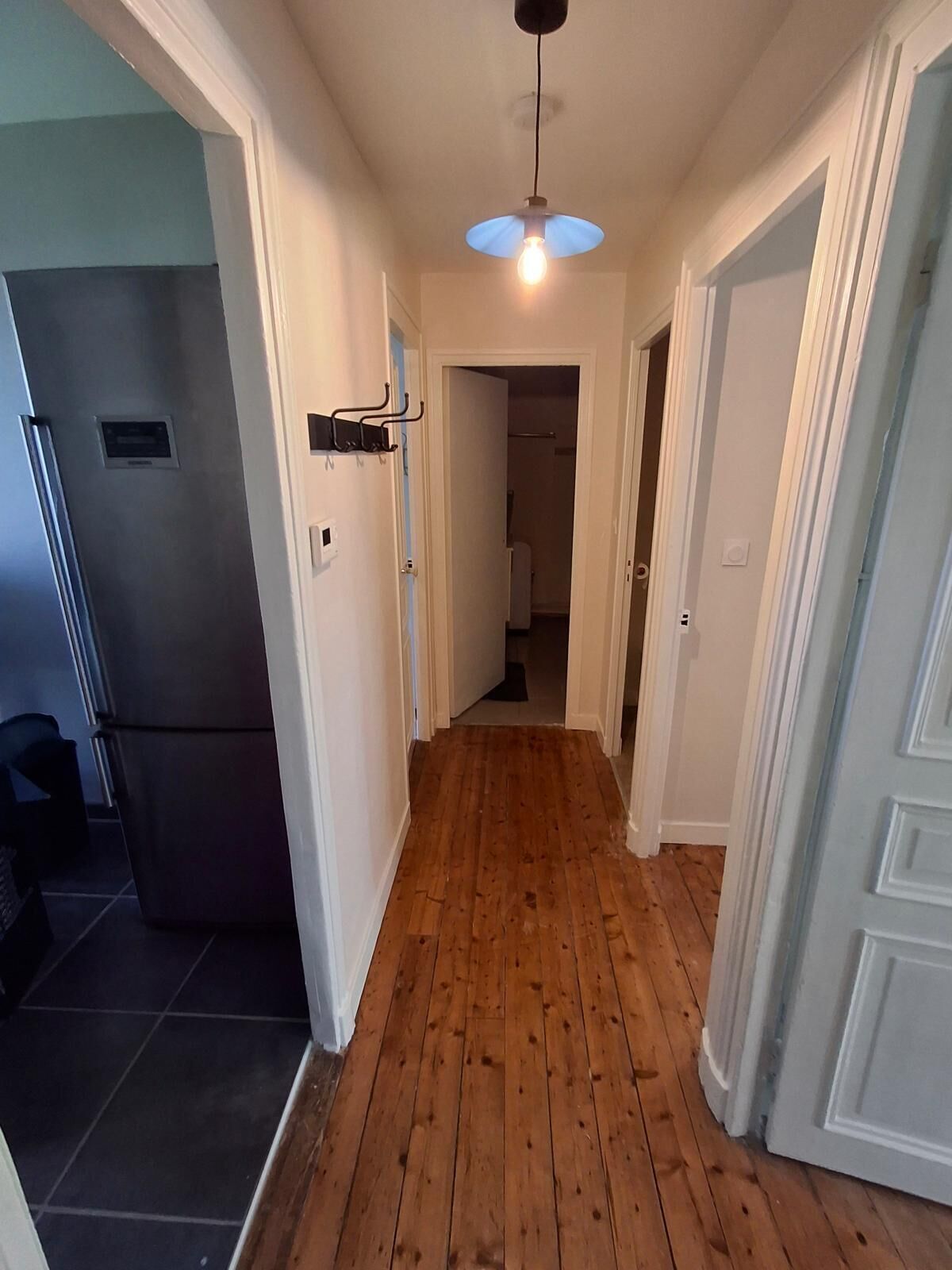 Un couloir doté d’un plancher en bois, de murs blancs et d’un luminaire au plafond.