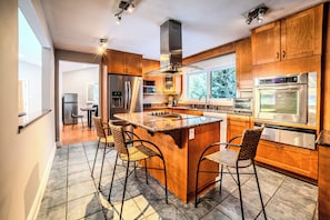 A modern kitchen with wooden cabinets, stainless steel appliances, and a central island with bar stools. - 6 Bedroom Main House XIV: SB (Carling)