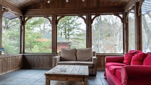 En overdækket veranda med træbjælker, en beige sofa, en rød sofa og et træbord.