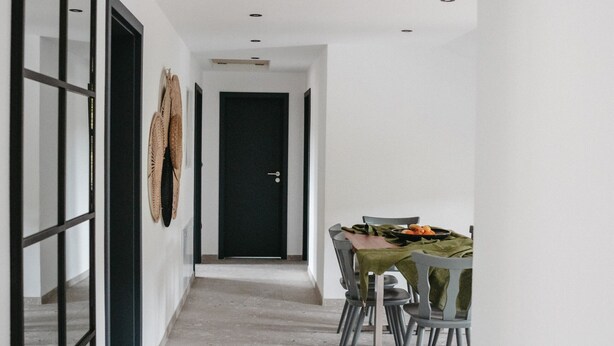A hallway leading to a dining area with a table and chairs, a door, and a wall-mounted circular decoration.