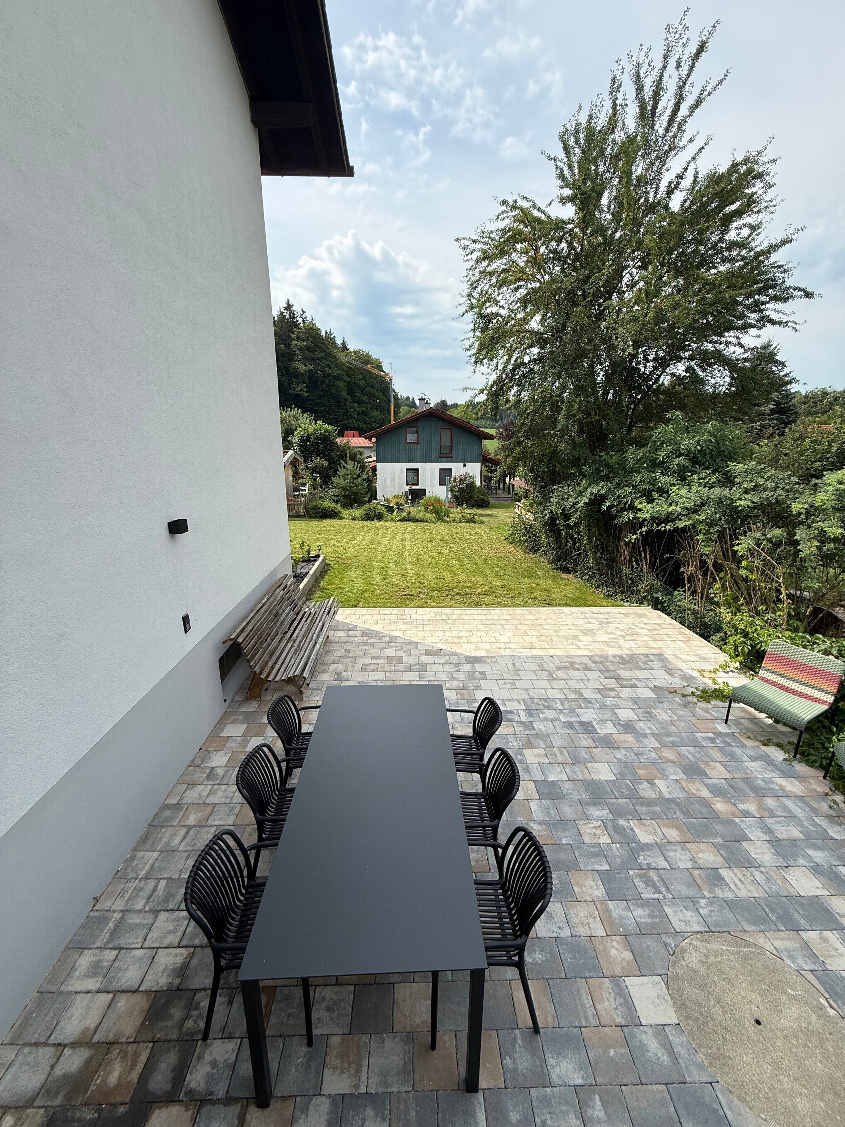 A patio with a table and chairs, a white wall, and a view of a house in the background.