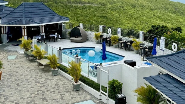 Un área de piscina en la azotea con piscina, sillas de descanso y mesas.