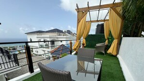 Un balcón con una mesa de vidrio y sillas de mimbre, con vistas a una piscina y edificios.