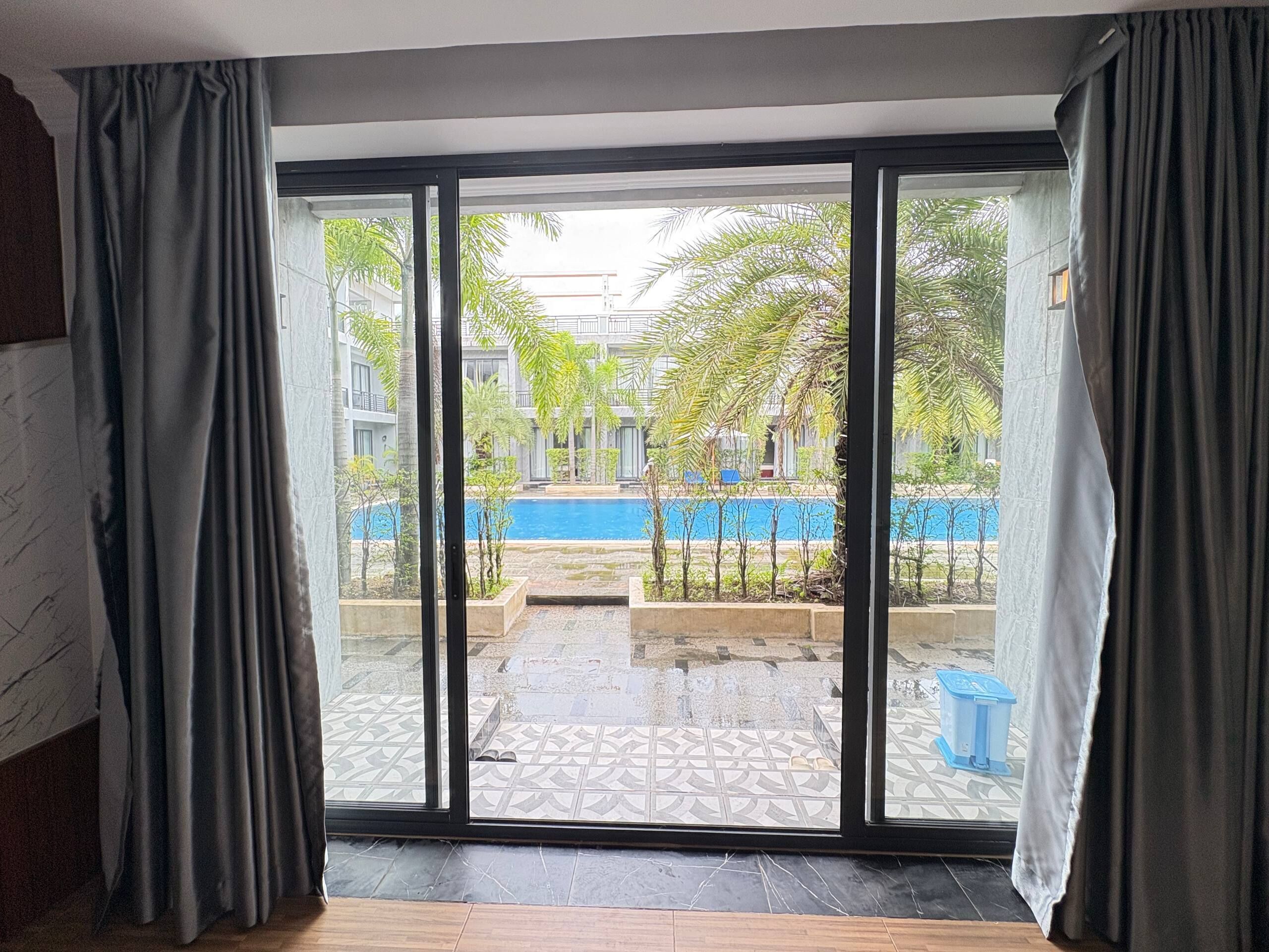 Una habitación con un amplio ventanal corredera que da a un patio con piscina y palmeras.