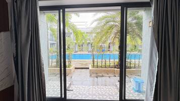 Una habitación con un amplio ventanal corredera que da a un patio con piscina y palmeras.