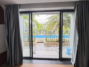 Quarto com uma grande porta de vidro deslizante que dá para um pátio com piscina e palmeiras.