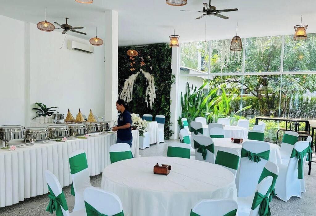 Un salón de banquetes con mesas redondas, manteles blancos y cintas verdes en las sillas.