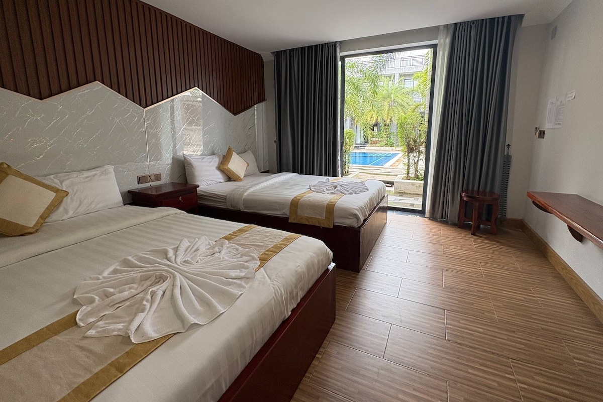A hotel room with two beds, a wooden floor, a view of a swimming pool, and a balcony.