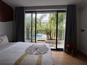 Quarto de hotel com uma cama grande, vista para uma piscina e piso de madeira.