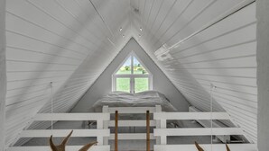 Una habitación con techos inclinados, una ventana que da a zonas verdes y una cama con colcha estampada.