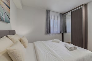 A neatly made bed with pillows and a rolled towel, a large mirror, and a painting on the wall. - Zadar Family Residence (Zadar)