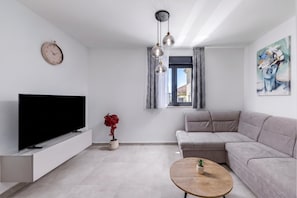 A modern living room with a flat-screen TV, a sofa, a coffee table, a potted plant, and a painting on the wall. - Zadar Family Residence (Zadar)