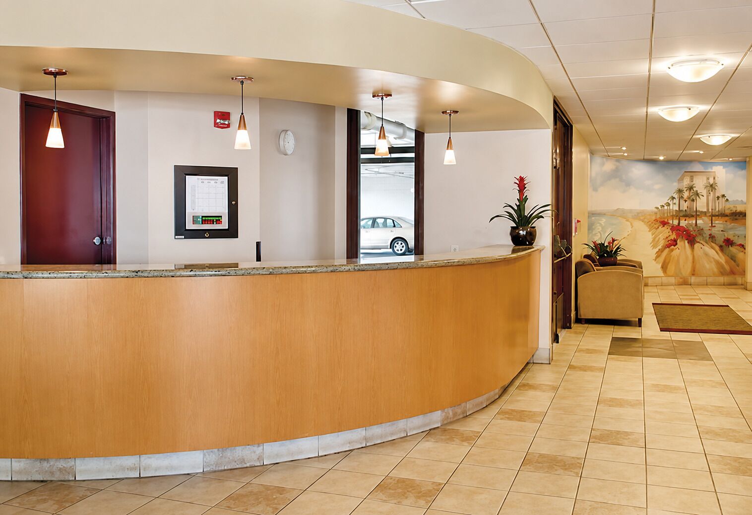 A reception desk with a wooden counter, a digital display, and a mural of a beach scene.