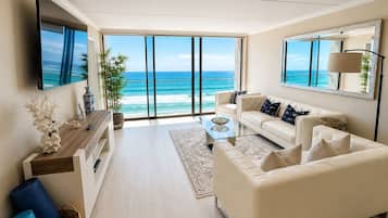 A modern living room with a large window overlooking the ocean, a flat-screen TV, a sofa, and a coffee table.