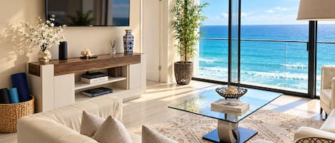 A modern living room with a large TV, a sofa, a coffee table, and a view of the ocean.