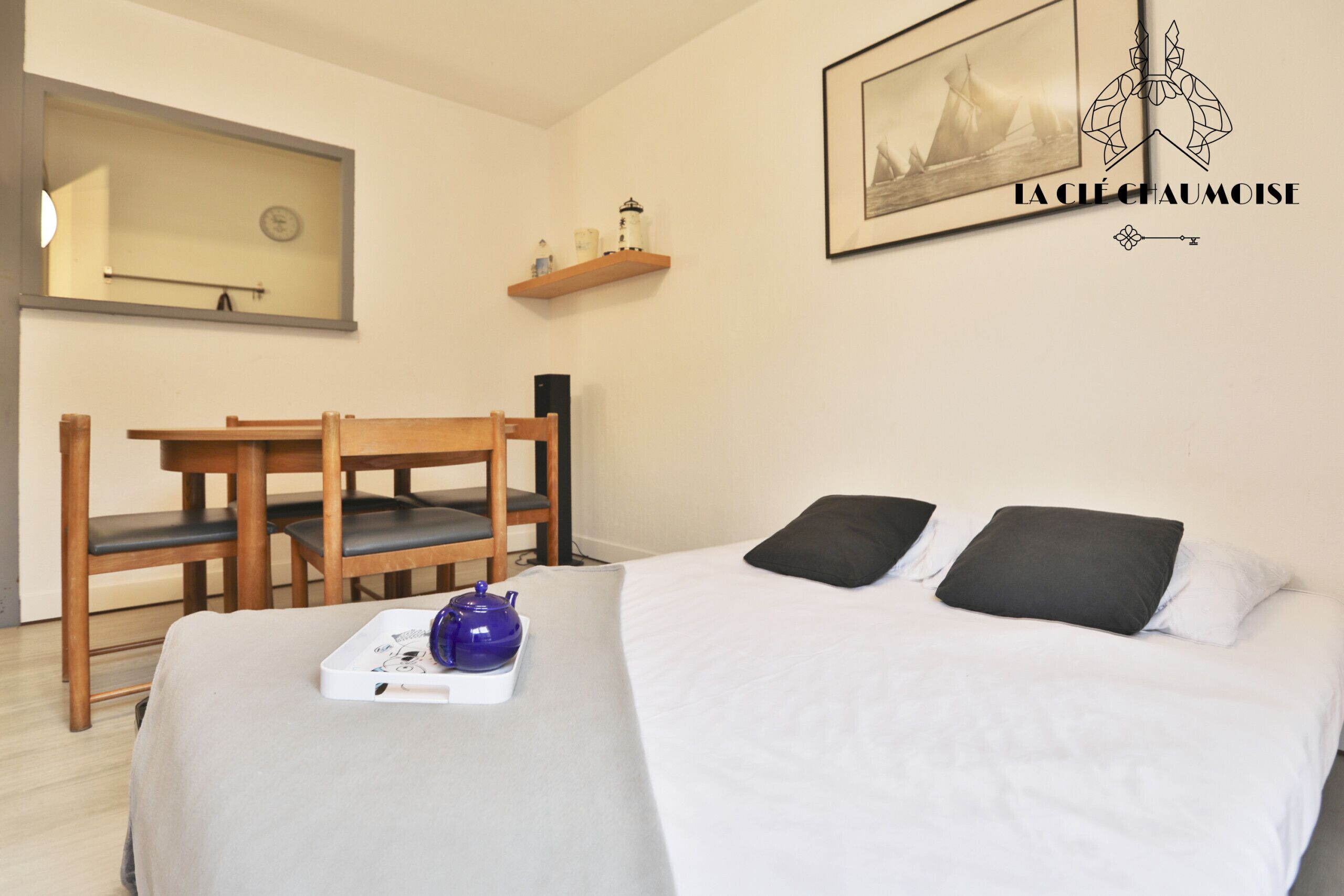 Un dormitorio con cama, escritorio, silla, espejo y estante con objetos decorativos.