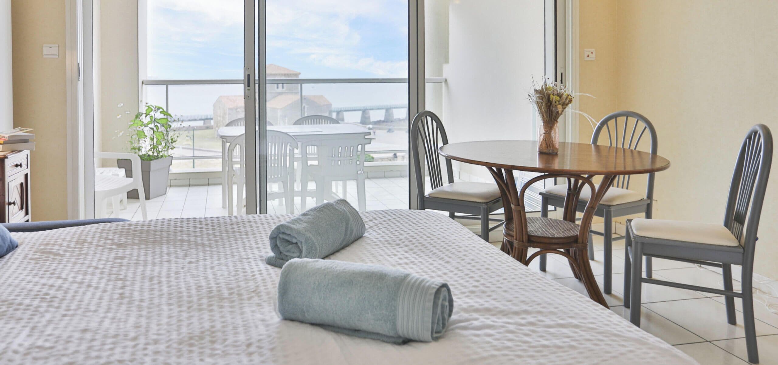 A hotel room with a large bed, a balcony with a table and chairs, and a view of the cityscape.
