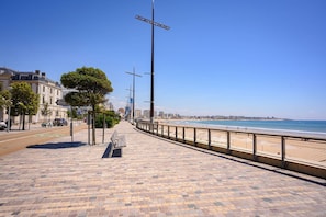 Une promenade dallée avec un banc, une plage et un ciel dégagé.