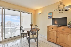 A room with a dining table, chairs, a TV, a cabinet, and a sliding glass door leading to an outdoor area. - Ancora 6  Studio avec vue sur la baie des Sables-d’Olonne (Les Sables-d´Olonne)