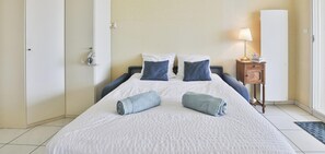 A hotel room with a bed, pillows, a bedside table with a lamp, and a door. - Ancora 6  Studio avec vue sur la baie des Sables-d’Olonne (Les Sables-d´Olonne)