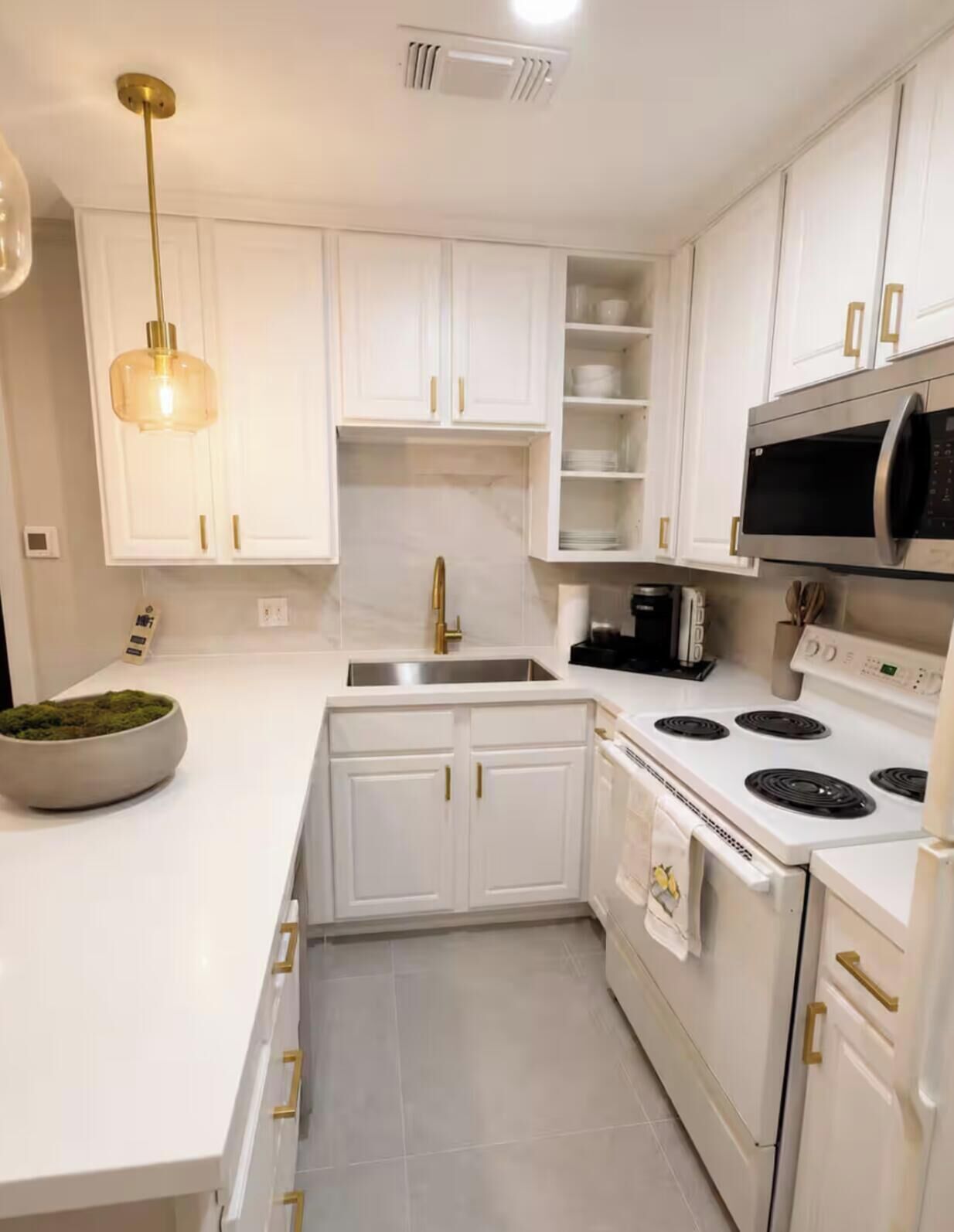 Een moderne keuken met witte kastjes, een roestvrijstalen spoelbak, een inbouwmagnetron en een gasfornuis.