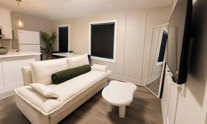 A compact living space with a sofa, a small table, a TV, and a kitchen area. - Houston Walkable Gem • Modern Montrose Stay (Houston)
