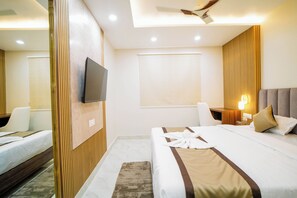 A hotel room with a bed, bedside table, lamp, and a TV mounted on the wall. - Hotel Kanishka Inn (Varanasi)