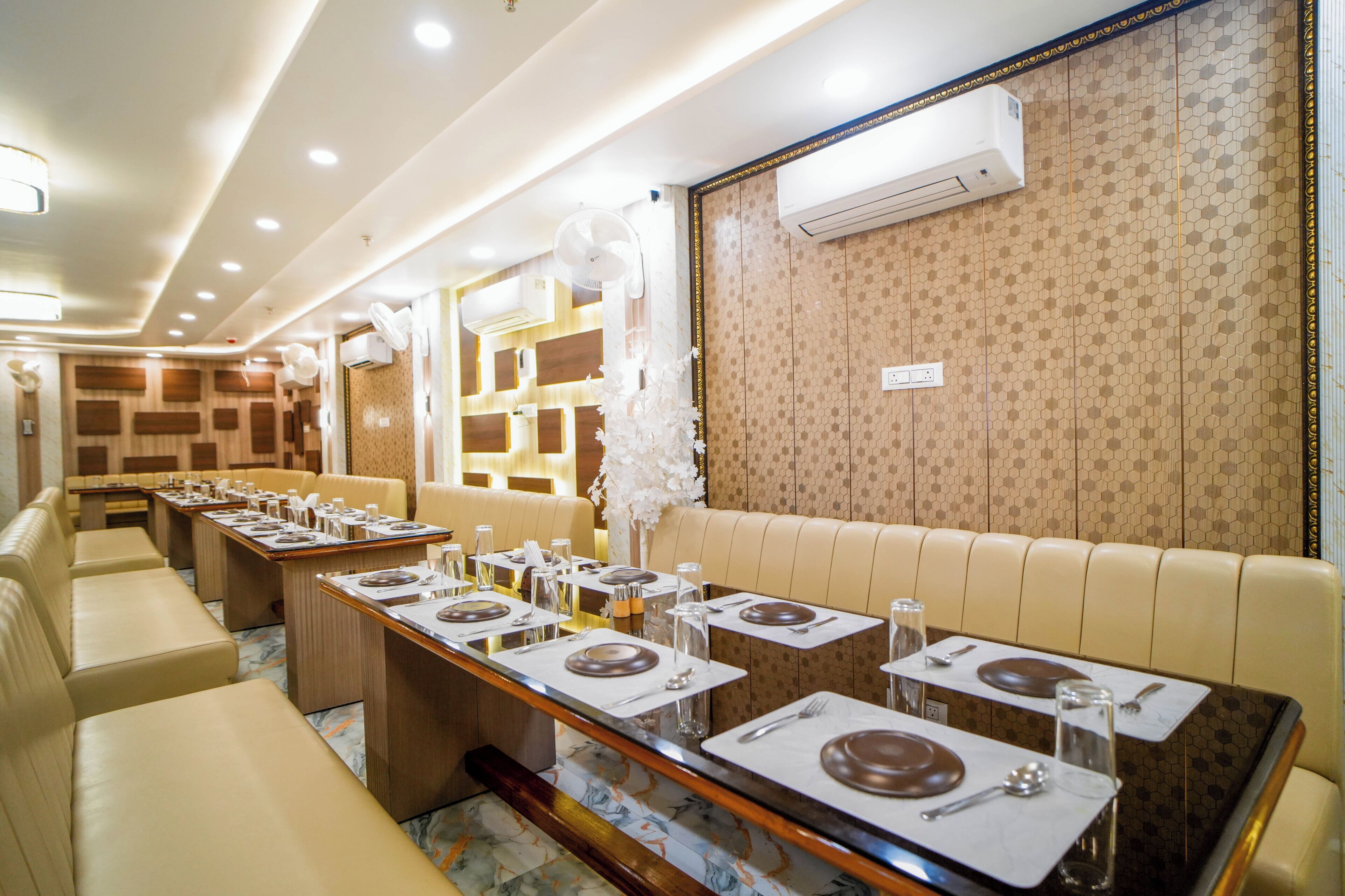 Un restaurante con mesas largas, asientos color beige y papel tapiz estampado.