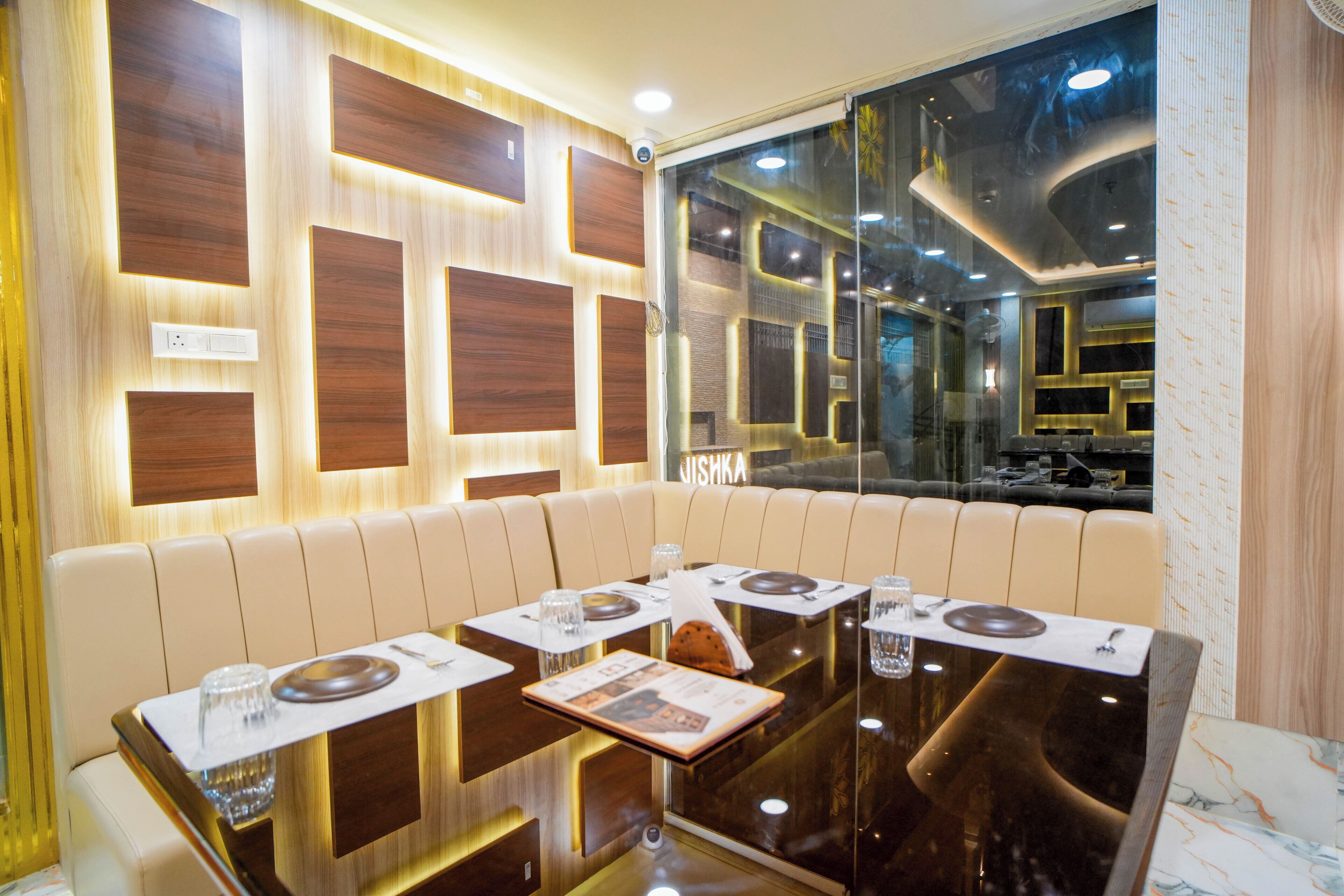 Een restaurant met een modern interieur, bestaande uit een glazen scheiding, een wand van houten panelen en een zithoek met tafels en stoelen.