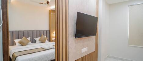 A modern hotel room with a bed, a mounted TV, and a wooden panel wall.
