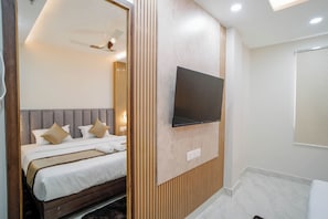 A modern hotel room with a bed, a mounted TV, and a wooden panel wall. - Hotel Kanishka Inn (Varanasi)