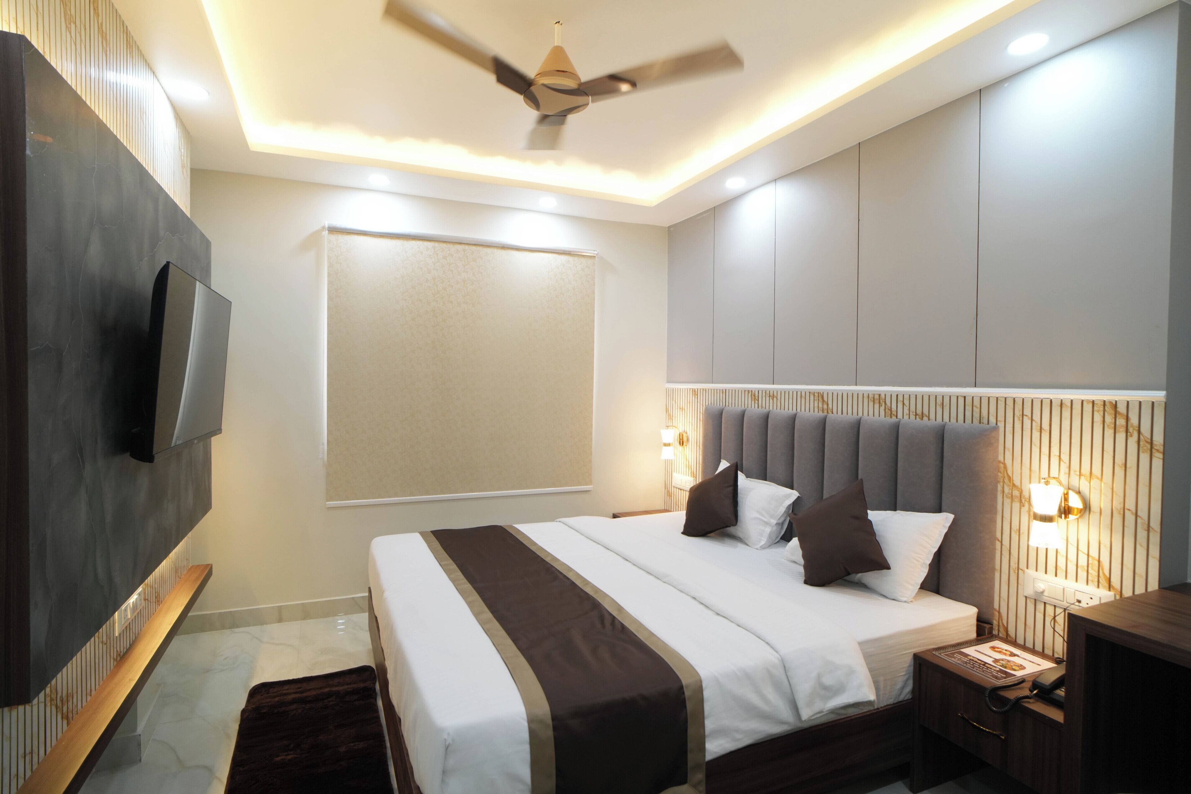 A modern bedroom with a bed, bedside tables, a TV, and a ceiling fan.