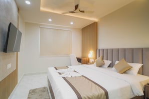 Habitación de hotel con cama, un televisor de pantalla plana montado en la pared, ventilador de techo y ventana con persiana.