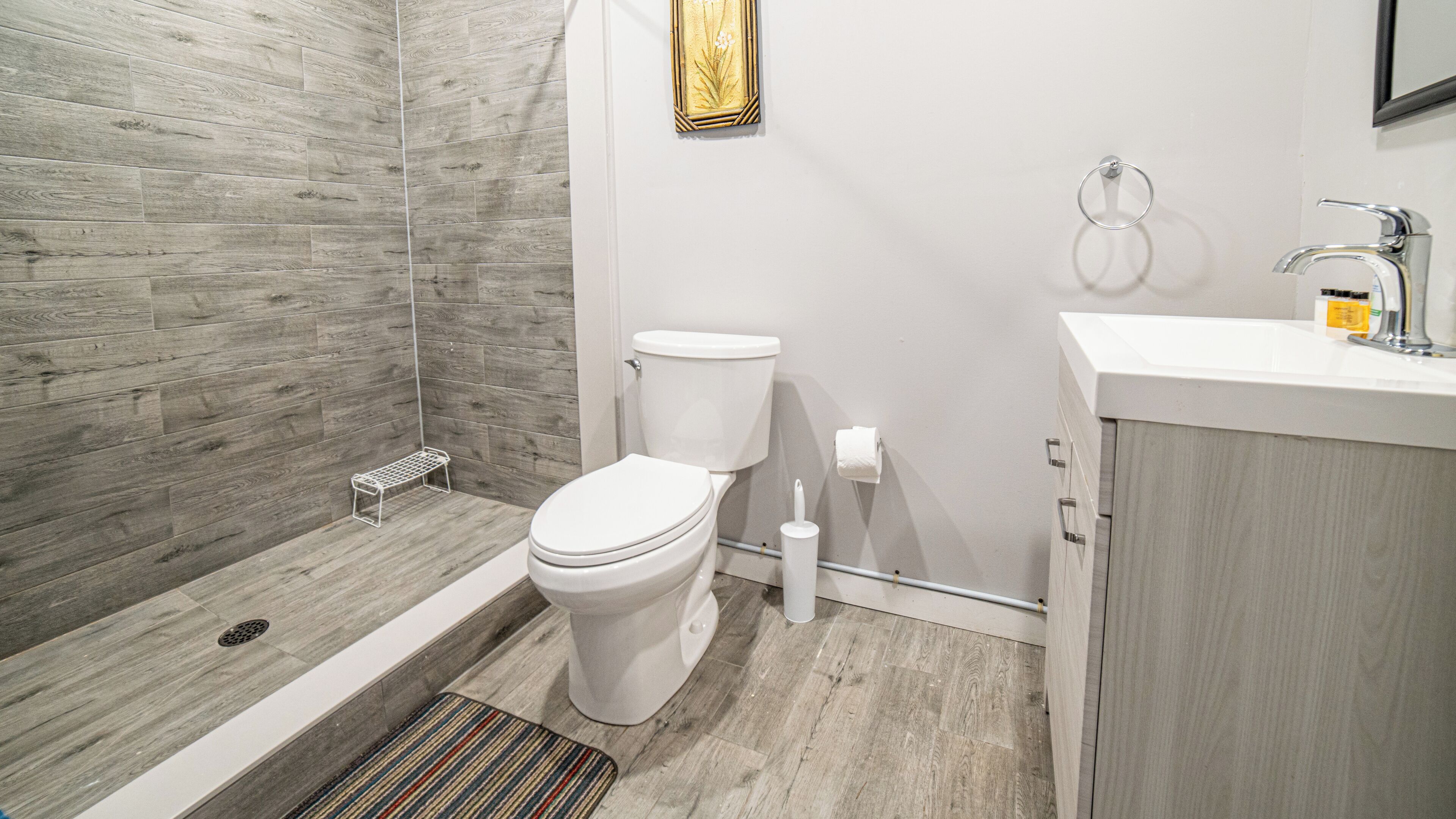 A modern bathroom with a shower, toilet, sink, and a small bench.