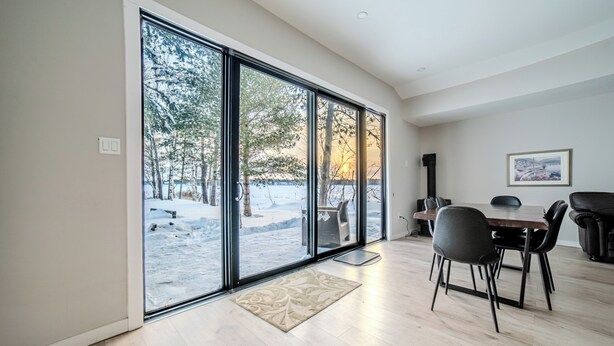 Une pièce spacieuse dotée de grandes portes-fenêtres coulissantes donnant sur un espace extérieur enneigé, d’une table à manger avec des chaises et d’un tableau encadré accroché au mur.