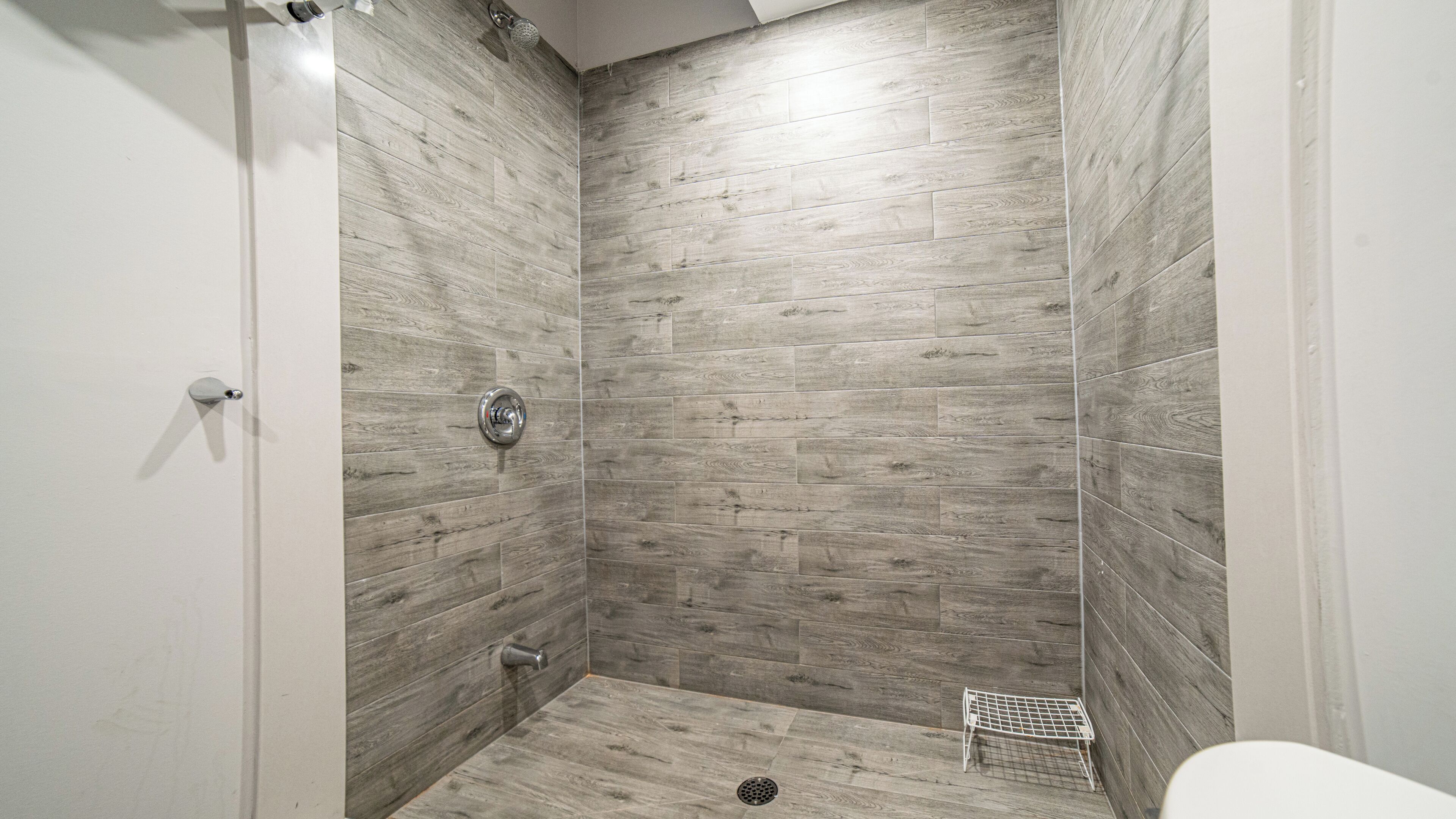 A shower with wooden tiles, a metal shower head, and a small metal shelf.