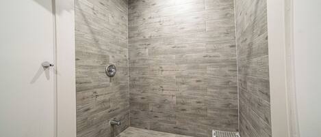 A shower with wooden tiles, a metal shower head, and a small metal shelf.