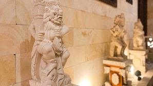 Una escultura de piedra de una deidad con tallado intrincado, frente a una pared de azulejos en un templo o edificio histórico.