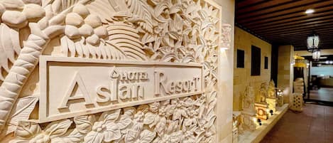 A carved wall with 'Hotel Aslan Resort' sign, intricate floral and leaf patterns, and a tiled floor.