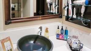 Un baño con un espejo grande, un lavabo con un recipiente decorativo y varios artículos de tocador sobre el mostrador.