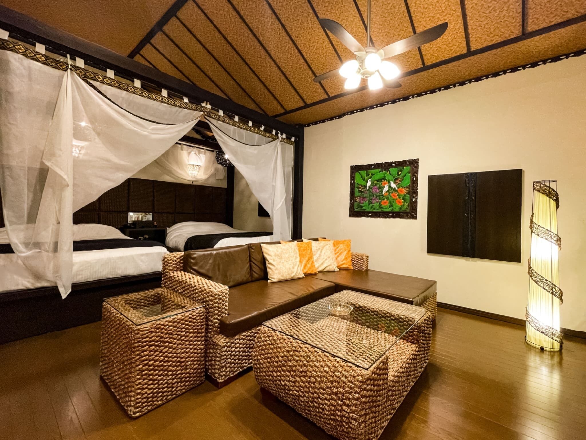 Una habitación con una cama bajo dosel, un sofá con cojines, una mesa de centro tejida y una obra de arte colgada en la pared.