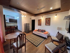 A compact living space with a dining area, a sofa with cushions, a television, and a ceiling fan. - Rustic Pines (Solan)