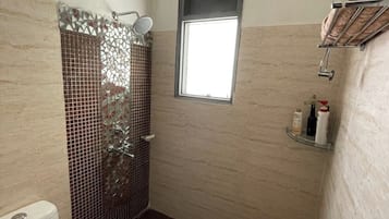 Um banheiro pequeno com vaso sanitário, chuveiro com porta de vidro, janela e prateleira com produtos de higiene pessoal.